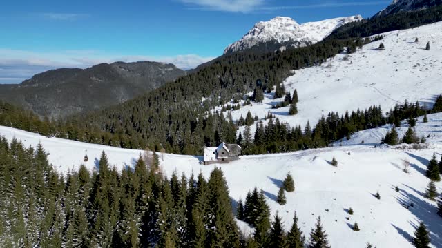 Ascending drone shot of an old cabin on a snowy hiking trail in the Bucegi Mountains, Romania