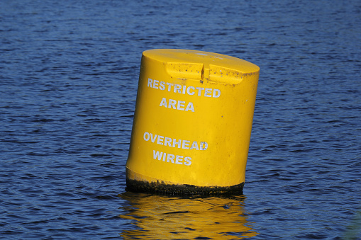 Yellow buoy floating on water with text written on it to indicate a restricted area due to overhead wires