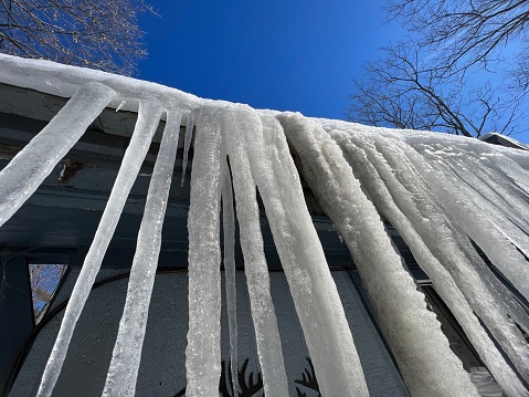 Icicles hang on the roof of a house against a bright blue sky. Spring landscape with icicles hanging from the roof of the house