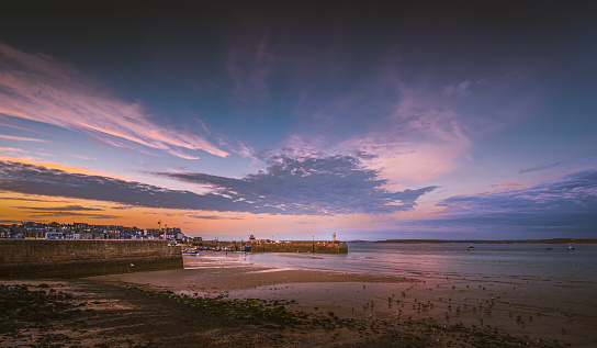 Dramatic view of beach and pier in seaside town St. Ives, Cornwall, England, in low tide at sunset with dramatic sky in background