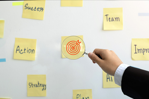 Targeting the business concept.business hand holding magnifying glass with a red target in the center with keywords.Business achievement goal and objective target. business strategy and Action plan