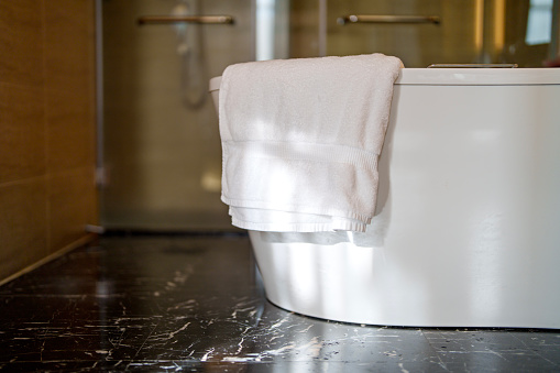 A used bath towel is placed on the edge of a bathtub, ready to be hung up or washed after use. This image suggests the completion of a bath or shower and the need to tidy up the bathroom area.