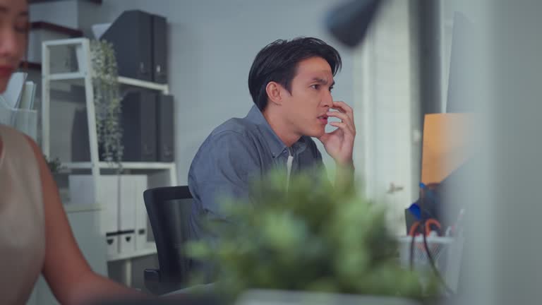 Serious asian businessman thinking about a solution to a problem while sitting in front of computer at a workplace in a modern office.