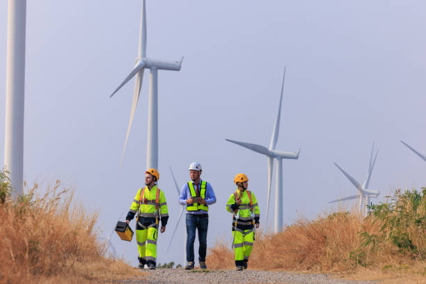 istock Engineers and inspector team wearing uniforms and helmets with equipment walking exploring and repairing electric wind turbines which are renewable energy for communities and agriculture. 2026884321
