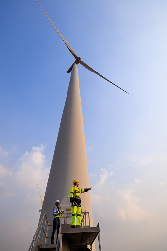 Engineer team hold using tablet standing to talk planing project in the wind turbines farm. renewable energy installation project for the future world concept. wide angle shot