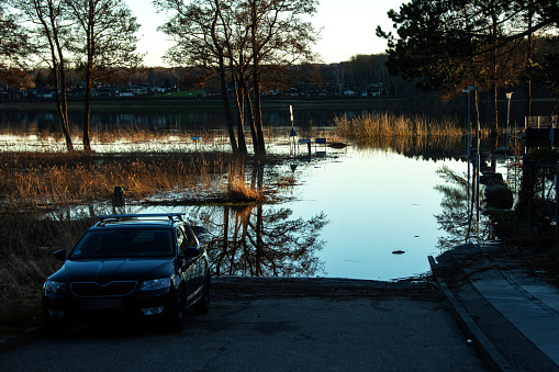 Flooding of a road as a lake in the city has overflowed its banks and a car is stopped just before the water
