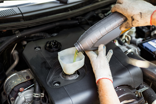 Changing the engine oil. A car mechanic pours oil from a bottle through a funnel into the engine filler neck.