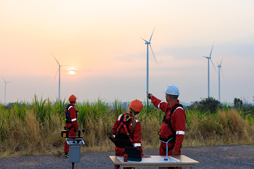 Engineer team standing looking down blueprint on the table to meeting planing project install wind turbines in agricultural sugarcane plantation area, in the morning sunlight background,