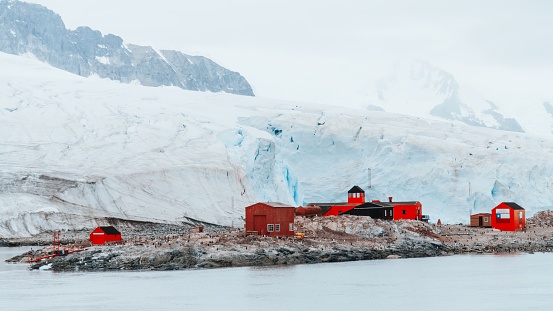 Antarctica Scientific Research Station at the coast of King George Island in front of huge Glacier. XPAN Panorama of vibrant orange-red painted Research Station and Rescue Huts and Houses at the Coast towards the Antarctic Ocean, Dallmann Bay, King George Island - Melchior Islands, Antarctica