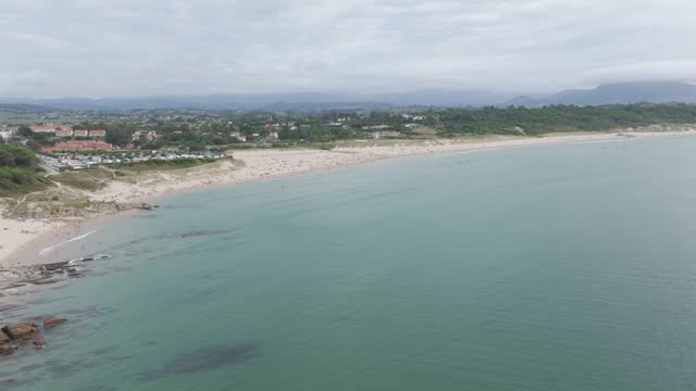 Rock formations enter the ocean at Playa De Somo beach in Santander Cantabric northern coast of Spain, Aerial pan left shot