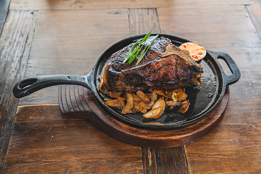 Meat chop in pan garnished with leek with spicy dipping sauce and baked potato on wooden table