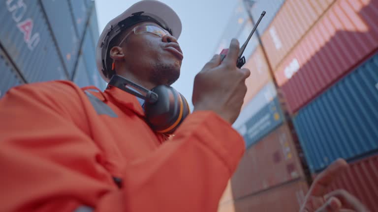 Warehouse worker speaking on a walkie talkie with a coworker in an empty container warehouse to inspect work.