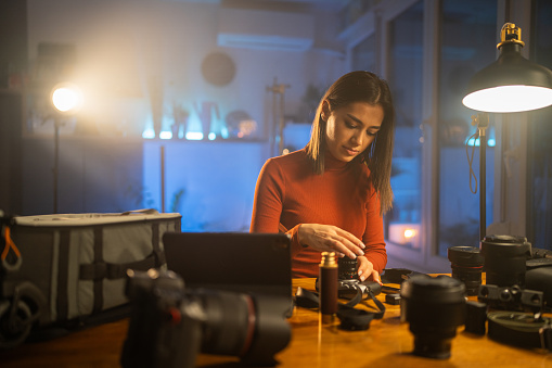 Young female photographer disassembling her photographic equipment under neon lights at home in the evening