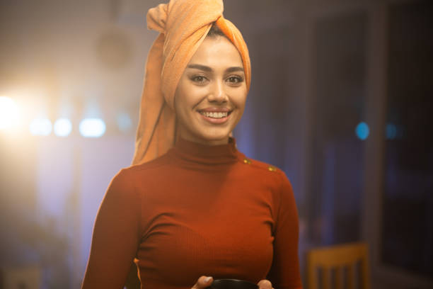 Beautiful young woman with towel on her head   holding remote control while watching TV at home late at night