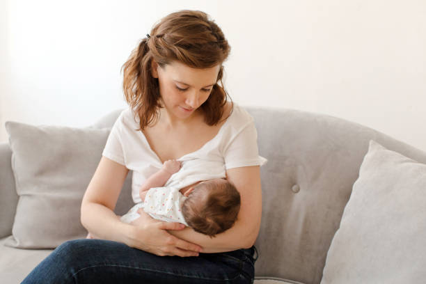 istock Happy mother breastfeeding baby sitting on sofa 2027055528