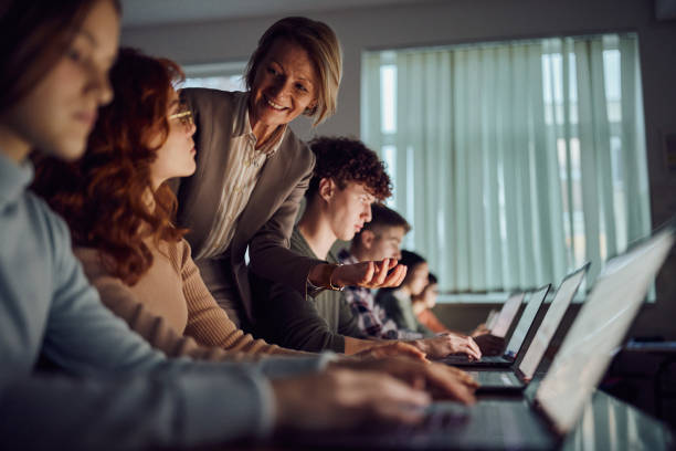 istock Happy mature professor assisting students in e-learning over computers at high school. 2027080913