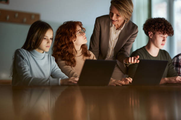 istock Happy senior teacher talking to her students in a computer lab. 2027082533