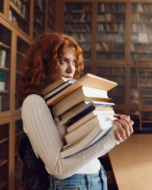 istock Redhead female student holding stack of books in library. 2027086214
