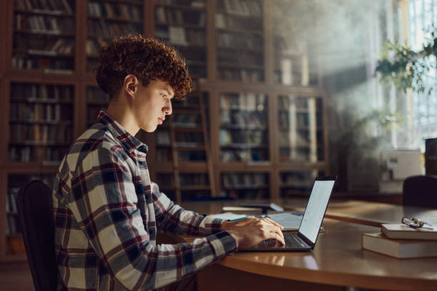 istock Teenage male student using laptop in library. 2027089373