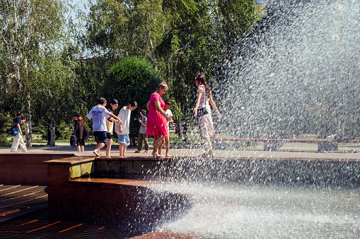 children and adults refreshing themselves in city fountain in urban park in Pavlodar, Kazakhstan 9.7.23