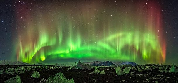 Panoramic view of the aurora borealis illuminating and coloring green the large blocks of ice on the black sand beach known as Diamond Beach at the estuary of the Jokulsarlon glacier, Iceland.