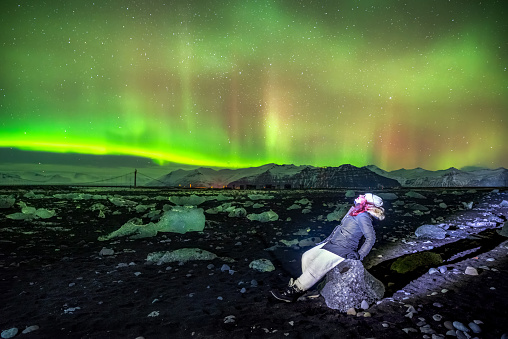Woman enjoying the Aurora borealis in Iceland at Diamond beach, Jokulsarlon glacier