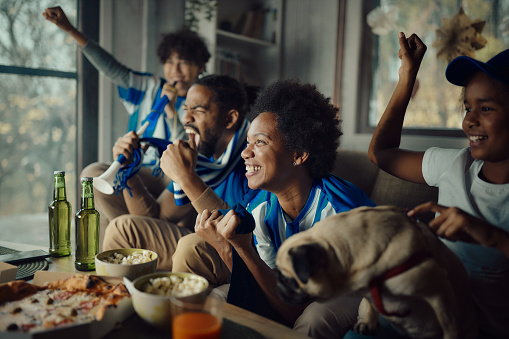 Cheerful African American family celebrating success of their soccer team while watching a game on TV at home.