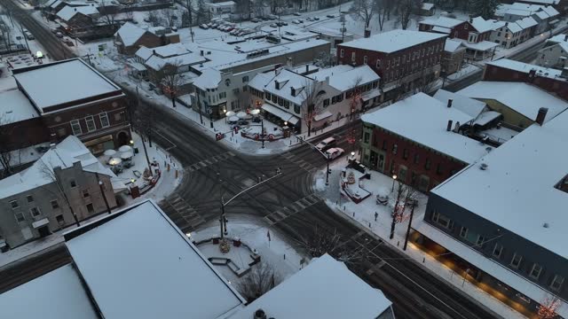 Small town square covered in snow at night. Christmas lights and decorations line American town. Aerial view of white Christmas in quaint USA town.