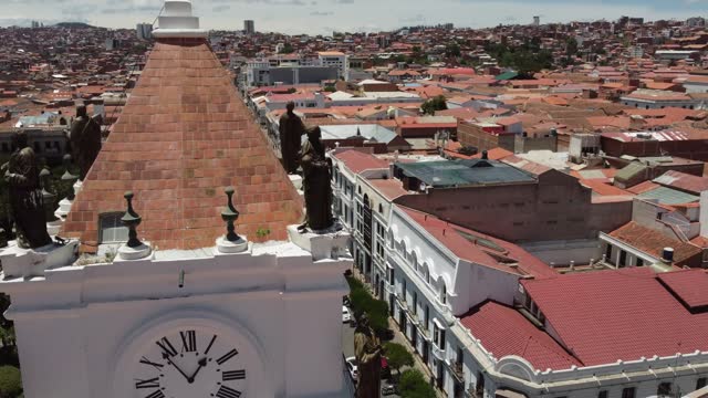 Aerial closely orbits clock tower statues on Sucre Basilica in Bolivia