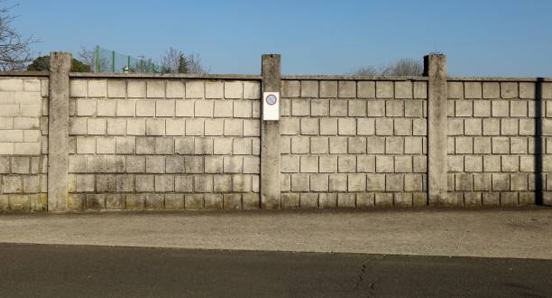 mur en blocs de béton avec un panneau d’interdiction d’arrêt au milieu. route goudronnée en face et ciel bleu au-dessus. - copy space road sign sky above photos et images de collection