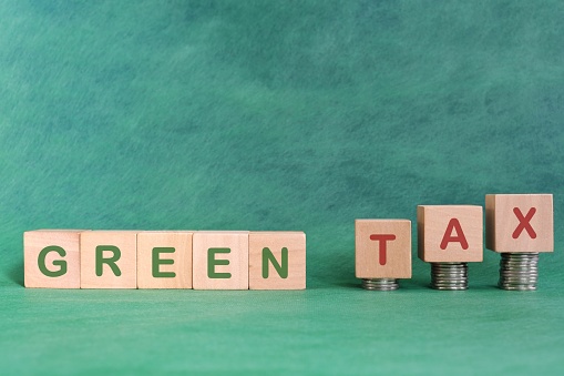 Green and environmental tax concept. Word in wooden blocks with increasing stack of coins.