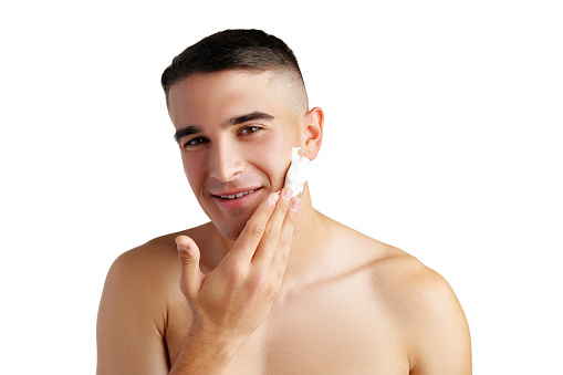 Young handsome man applying shaving foam against white background in studio