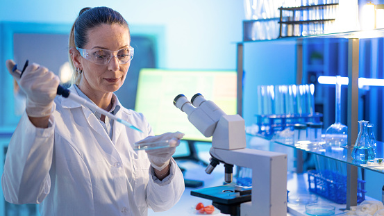 Female research scientist is analysing a sample on her microscope in a microbiology lab