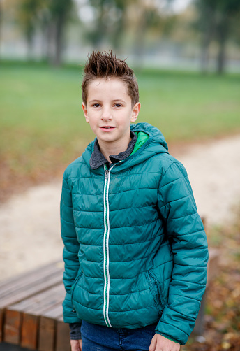 Cute preadolescent boy in autumn jacket playing in public park, autumn leaves on the ground, outdoor pursuit and leisure time