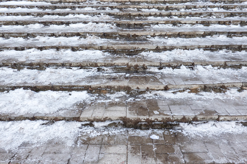Close-up of the stairs going up. The gray tile steps are covered with a layer of ice and snow. There is a well-trodden path in the middle. Background.