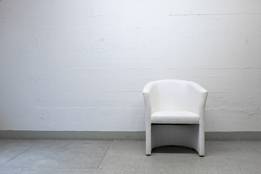 Old vintage, well-used white leather armchair set against grungy concrete wall, no people.