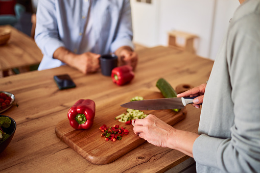 A close-up shot of a senior adult female hands cutting vegetables on a wooden cutting board and preparing a salad in a domestic kitchen.