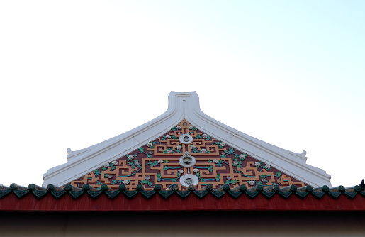 Ancient native Chinese style art in Thailand on isosceles triangle shape gable of church in temple white sky background. White cement rim and brown geometric pattern design on gable.