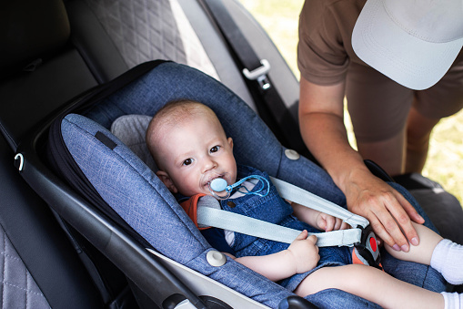 A baby boy is sitting in a baby car seat in a car. The concept of safety when transporting small children in a car