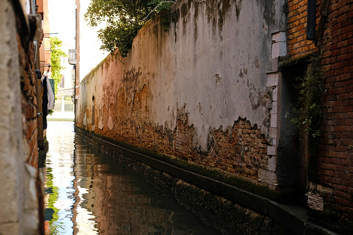 Typical narrow streets and canals between сolorful and shabby houses in Venice, Italy. Historical architecture in Venice, parked boats on the canals.