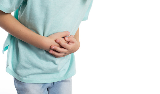 A child holds his stomach with his hands on a white background, close-up. Abdominal pain in children due to helminths, weight loss and poor health. Copy space for text