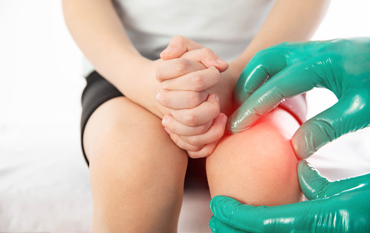 A doctor traumatologist orthopedist examines the knee joint of a child who has knee pain. Concept of growing pains in children. Dislocation and injury of the knee, sprain, musculoskeletal system