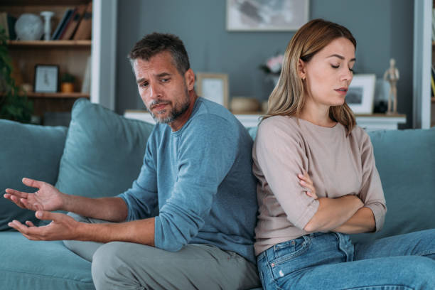 Unhappy young couple Shot of a young couple having a disagreement at home. Couple ignoring each other while sitting back to back on the couch. Man and woman with relationship problems sitting on sofa and not talking to each other. arguing stock pictures, royalty-free photos & images