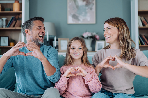 Shot of a cheerful family making heart shapes with hands while sitting on the sofa at home.