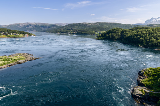 The dynamic Saltstraumen tide, captured from above, with its powerful whirlpools contrasting against the serene Nordic scenery and residential areas