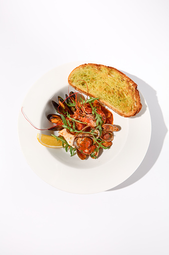 SautÃ©ed seafood medley in tomato sauce with a side of ciabatta toast on a white plate, top view for a delightful seafood experience.