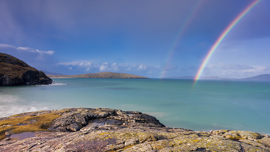 Rainbows in the sky above the turquoise sea on the Isle of Harris, Scotland
