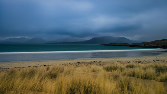 A rain shower passes over the distant mountains giving moody light on Luskentyre Beach