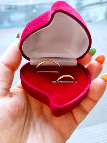 the girl holds in her hand a red box with two engagement rings for the wedding proposals wedding preparations morning of the bride, red heart shaped velvet box