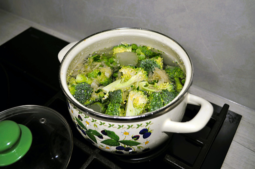 white pan on an induction stove with soup made from pieces of broccoli, cabbage, cauliflower, herbs, vegetables, vegetarianism and a lid with a green handle, kitchen, food preparation, broth